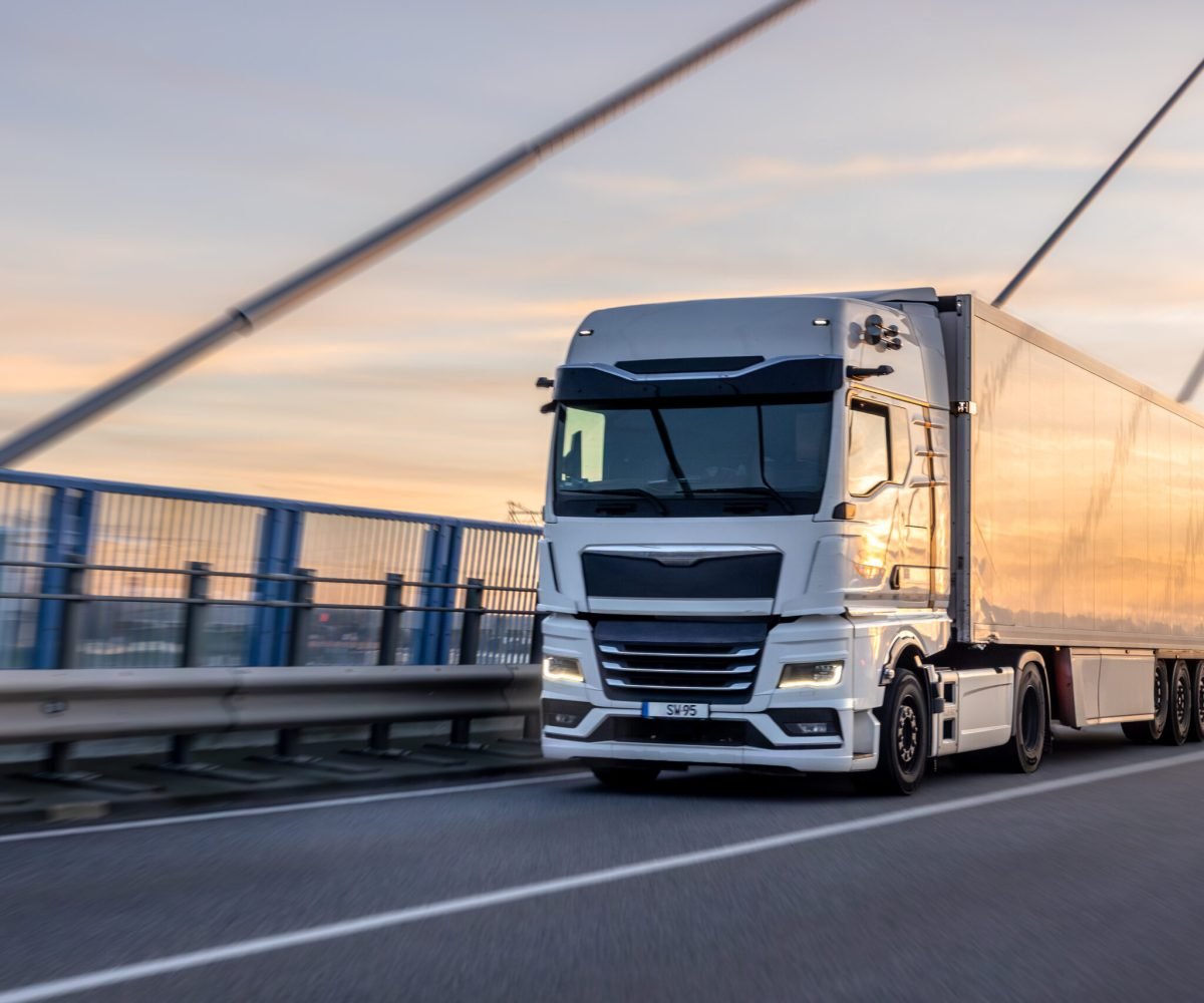 A powerful white freight truck drives over the modern bridge at golden hour. Concept of professional logistics, speed, and efficient transportation at sunset.